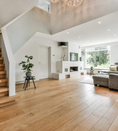 A cozy house interior with a wooden floor, large gray sofa, and stairs leading to the second floor